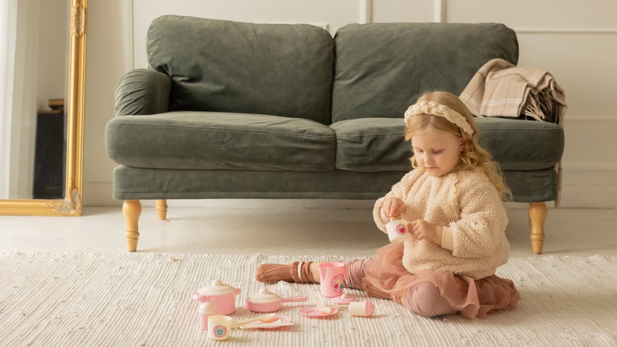 A young girl playing with a tea set in a cozy living room setting.